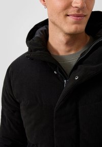 Giacca in corduroy nera con zip davanti, grande cappuccio e chiusura a pressione. Presenta una texture a coste e dettagli in metallo argentato.