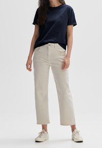 T-shirt in cotone navy con scollo rotondo, indossato sopra jeans beige chiaro alla caviglia con orli sfilacciati, abbinati a sneaker bianche.