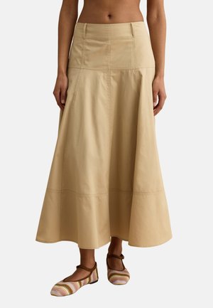 Falda midi beige de cintura alta en corte línea A, combinada con zapatos Mary Jane marrones con rayas multicolor, en una modelo descalza.