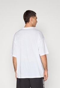 Hvit bomulls t-skjorte med rund hals, korte ermer, avslappet passform, og uten synlige logoer eller mønstre. Bakfra viser den et enkelt, rent design.