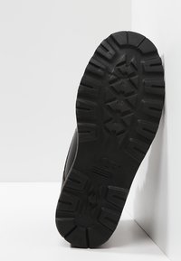 Suela de bota de goma negra con un patrón texturizado, que presenta surcos profundos y un logo de marca. Diseñada para ofrecer tracción y durabilidad.