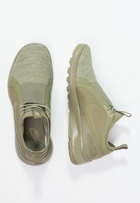 Olivově zelené sportovní boty s prodyšným síťovaným svrškem, hladkými plastovými akcenty, elastickým šněrovacím systémem a texturovanou gumovou podrážkou.