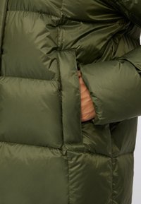 Giacca puffer verde scuro con design trapuntato, dotata di tasca laterale e texture liscia e lucida.