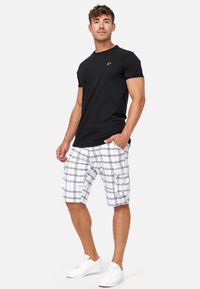 T-shirt noir à manches courtes avec un petit logo, associé à un short cargo à carreaux blancs avec des poches et des accents noirs. Baskets blanches.