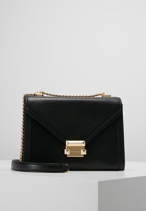 Sac à main rectangulaire en cuir noir avec anse chaîne dorée et fermeture à boucle dorée sur surface blanche sur fond gris.