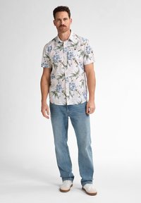 Camisa de flores de manga corta en rosa claro con flores azules y hojas verdes, combinada con jeans de mezclilla azul claro y zapatillas blancas.