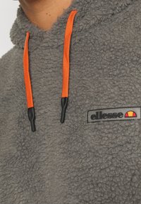 Sweat à capuche en polaire texturée grise avec des cordons de serrage orange vif et un patch logo de la marque ellesse sur la poitrine.