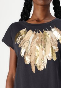 Black short-sleeve t-shirt featuring a gold and beige feather graphic print across the chest. Soft fabric with a relaxed fit.