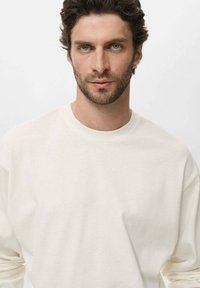 Light cream long-sleeve t-shirt made of soft fabric, featuring a classic crew neck and relaxed fit. Minimalist design with no visible patterns or accents.