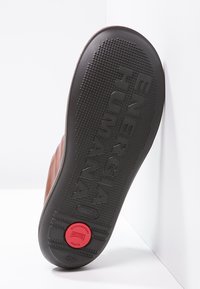 Semelle de chaussure en cuir marron avec grip texturé, portant l'inscription gravée "ENERGIA HUMANA", un accent circulaire rouge et une indication de taille 40.