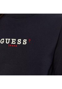 Navyblauwe sweatshirt met geborduurde tekst "GUESS?" en "jeans" in wit en rood. Beschikt over een geribbelde halslijn en een zachte stoftextuur.