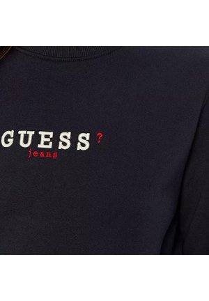 Felpa blu navy con ricamo della scritta "GUESS?" e "jeans" in bianco e rosso. Presenta un colletto a coste e una texture di tessuto morbido.