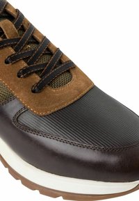 Sneaker en cuir marron avec un embout en caoutchouc noir texturé, des accents en suède, des lacets marron et une semelle intermédiaire blanche. Comprend un panneau en tissu respirant.