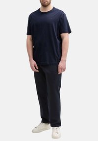 T-shirt en coton marine avec un col rond, associé à un pantalon foncé et des baskets blanches. Design simple, style minimaliste.