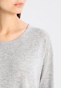 Vaalea harmaa neulepaita pyöreällä kaula-aukolla. Pehmeä tekstuuri, leveät hihansuut ja hieman rento istuvuus.