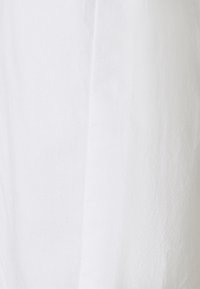 Tissu blanc texturé avec une couture verticale subtile et un motif de tissage fin visible sur toute la surface.