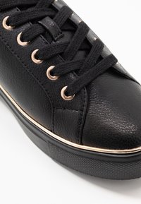 Black leather sneaker with textured finish, round toe, black laces, metallic eyelets, and a gold accent on the midsole.