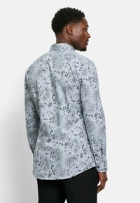 Herren Langarmhemd aus hellblauem Stoff mit aufwendigen schwarzen Paisleymustern, Punktkragen und abgerundetem Saumdesign.