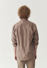 Cămașă bej cu mânecă lungă, cu o croială lejeră, guler cu nasturi și manșete răsfrânte. Material moale, texturat, cu detalii fine de cusătură.