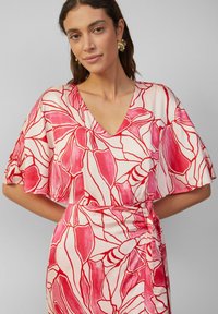 Blumenmusterkleid mit V-Ausschnitt, kurzen Flatterärmeln und einem taillierten Design in Pink und Cremefarben. Glatte Stoffstruktur.