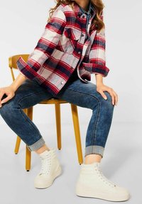 Rood en marineblauw geruite flanellen jas met knopen, gedragen over een spijkerbroek met lange mouwen, gecombineerd met donkere skinny jeans en witte hoge sneakers.