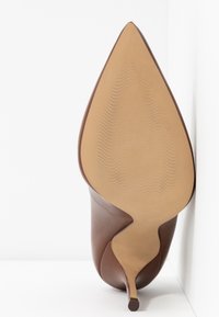 Chaussure à talon aiguille marron avec un bout pointu et une tige en cuir lisse. La semelle est beige avec un motif ondulé, soulignant un design élégant.