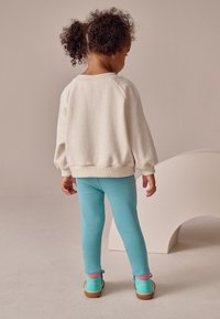 Felpa color crema, leggings blu e scarpe colorate con particolari rosa. Tessuto morbido, vestibilità comoda e maniche raglan visibili da dietro.