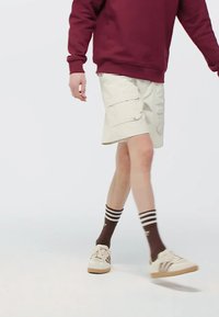 Bež cargo šortsi s više džepova, upareni s bordo duksericom, smešnim prugastim čarapama i krem tenisicama s gumiranim đonom.