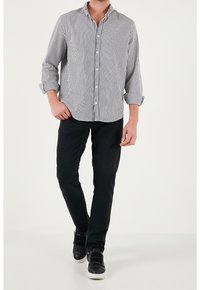 Gestreept zwart-wit langemouwen shirt met knoopsluiting, gecombineerd met zwarte jeans en zwarte sneakers. Casual en aansluitende silhouet.