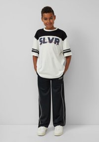 Witte en zwarte kortarmige shirt met 'SLVR' print, gecombineerd met zwarte broek met witte zijkanten en witte sneakers.