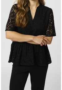 Top in pizzo nero con maniche corte, scollo alto e design a peplum; presenta motivi floreali e una finitura texture. Abbinato a pantaloni neri.