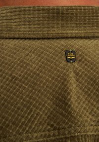Olijfgroen corduroy stof met een ribbelstructuur; heeft een zwart PME Legend logo-label dat dichtbij de kraag is bevestigd.