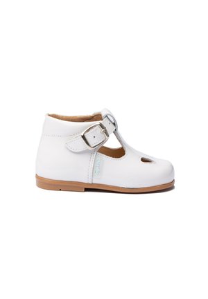 Zapato T-bar de cuero blanco con diseño cortado, correa ajustable con hebilla y suela de goma marrón. Textura minimalista y suave.