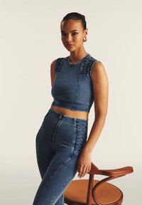 Denim crop top dengan aksen bahu yang berpola dan dikepang, dipadukan dengan celana denim pinggang tinggi yang memiliki ritsleting di bagian tengah dan detail samping.
