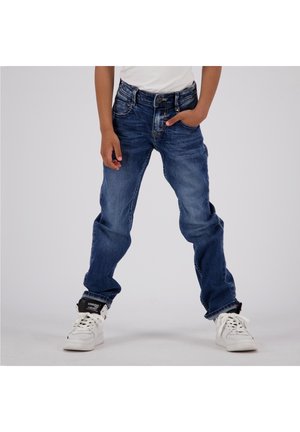Modré džíny z denimu s uvolněným střihem, pěti kapsami, vybledlými oblastmi a klasickým designem. Nosič má na sobě bílé vysoké tenisky.