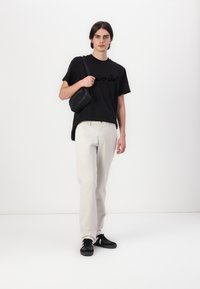 T-shirt noir à manches courtes avec un design script, pantalon beige, et baskets noires avec des rayures blanches. Sac à épaule en cuir noir.