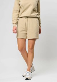 Beige shorts gemaakt van zachte stof, met een elastische tailleband met een trekkoord, zijzakken en een comfortabele pasvorm. Gecombineerd met witte sneakers.
