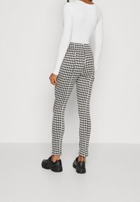Hoge taille zwart-wit houndstooth-patroon broeken, getailleerd ontwerp met een zachte textuur, gecombineerd met zwarte sportschoenen.