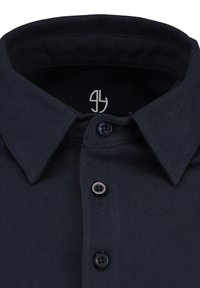 Dunkelblaues Baumwollhemd mit spitzem Kragen, das eine subtile Textur aufweist, eine Knopfleiste mit drei Knöpfen hat und ein kleines gesticktes Logo innen am Kragen trägt.