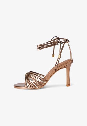 Metalen bronzen sandaal met hoge hak, dunne enkellussen die om de enkel worden gewikkeld en een open neus met meerdere smalle banden aan de voorkant.