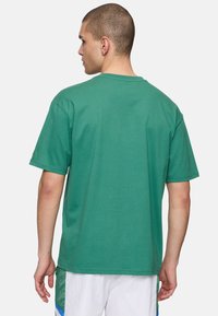 Camiseta de algodón verde con cuello redondo, mangas cortas y un ajuste relajado. Incluye un detalle de marca sutil en la manga izquierda.
