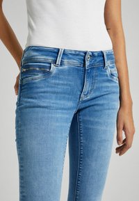 Světlé modré džíny z denimu s přiléhavým střihem, s přední kapsou na zip, středním praním a jemnými detaily vyblednutí.