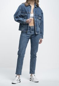 Denim jacket and jeans in light blue, featuring a relaxed fit, front pockets, and subtle texture. Paired with white sneakers.