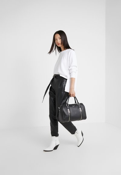 Schwarze Lederhandtasche mit silbernen Beschlägen, oberen Griffen und Nietenakzenten, kombiniert mit einem weißen Pullover und schwarzen Kunstlederhosen.