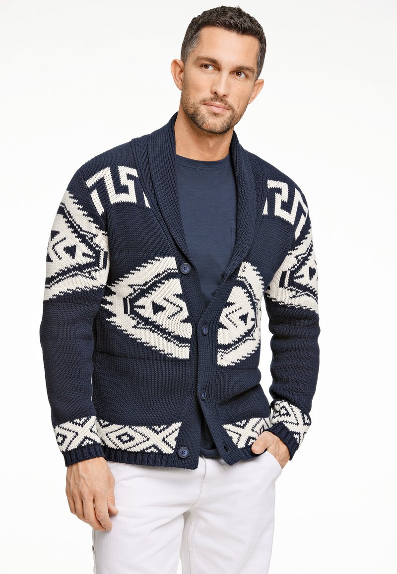 Marinblå stickad kofta med vita geometriska mönster, sjalkrage, knappstängning och ribbade manschetter. Avslappnad design med texturerat fabric.