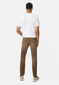 Bruine corduroy broek met een slim fit, zichtbare achterzakken en een licht gestructureerd oppervlak. Draagt een eenvoudig wit t-shirt en sneakers.