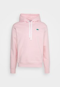 Světle růžová mikina s kapucí a bílými tkaničkami, klokaní kapsou, ribbovanými manžetami a malým zeleným krokodýlím logem na hrudi.