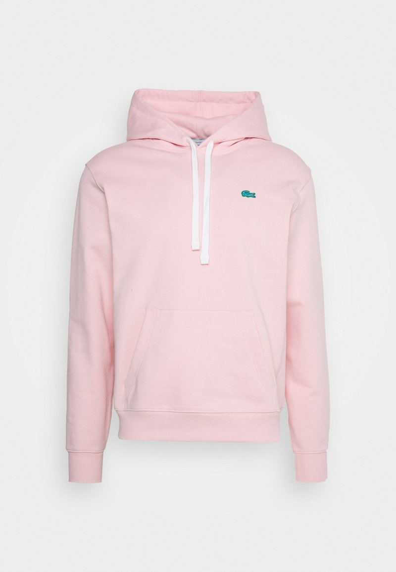 Ljusrosa huvtröja med vita snören, känguruficka, ribbade ärmslut och en liten grön krokodil-logotyp på bröstet.