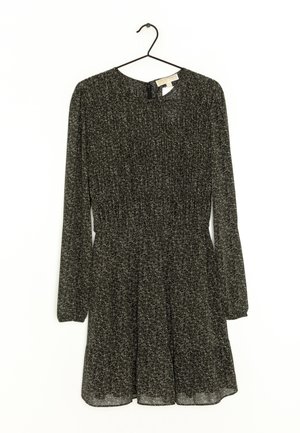 Robe longue noire à manches longues avec petit motif floral blanc, taille cintrée, encolure ronde et jupe légèrement évasée, suspendue sur un cintre noir.