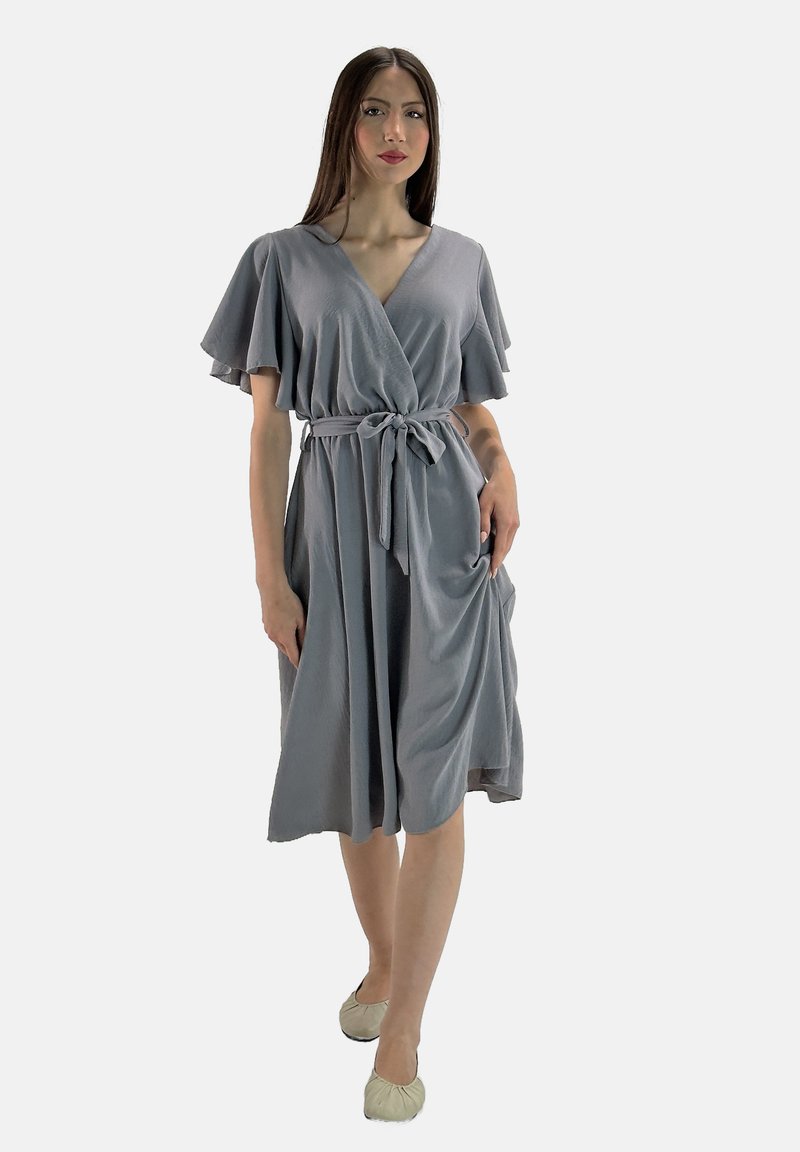 Robe grise à manches courtes et flottantes, nouée à la taille, avec une texture lisse et une longueur au genou. Portée avec des ballerines de couleur claire.